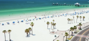 A white sandy beach lined with umbrellas and palm trees meets the blue ocean.